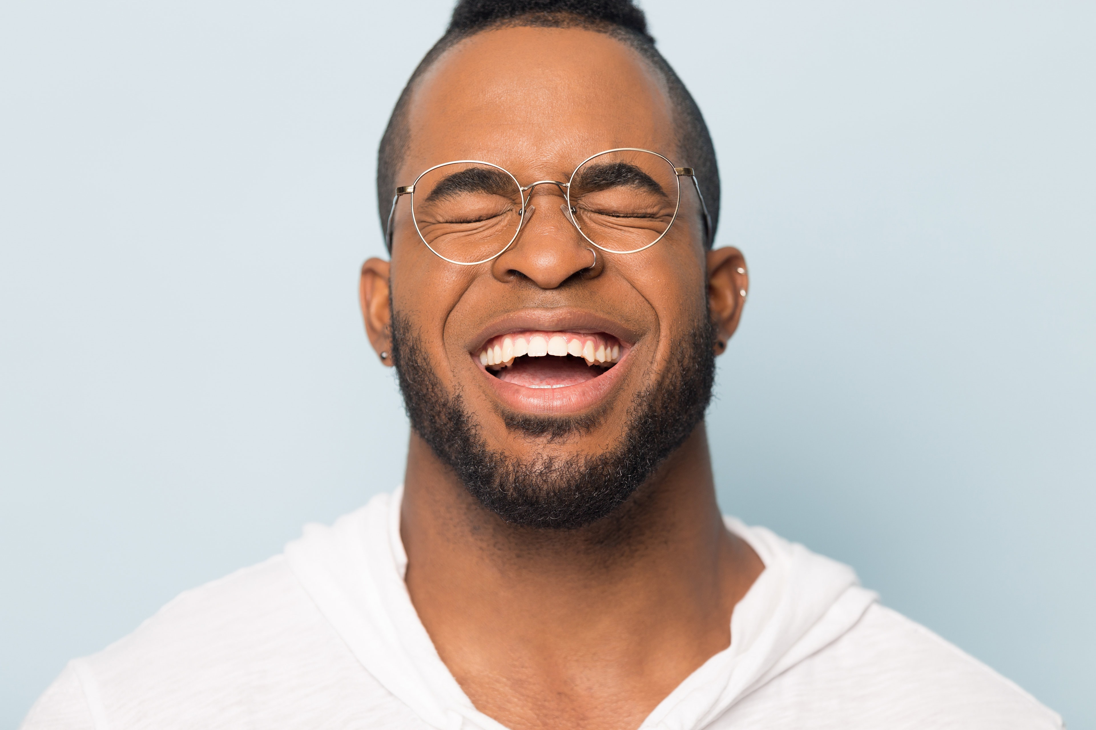 Close up of happy african American man in glasses isolated on blue studio background laughing with wide toothy smile, excited black millennial male in eyewear show healthy white teeth